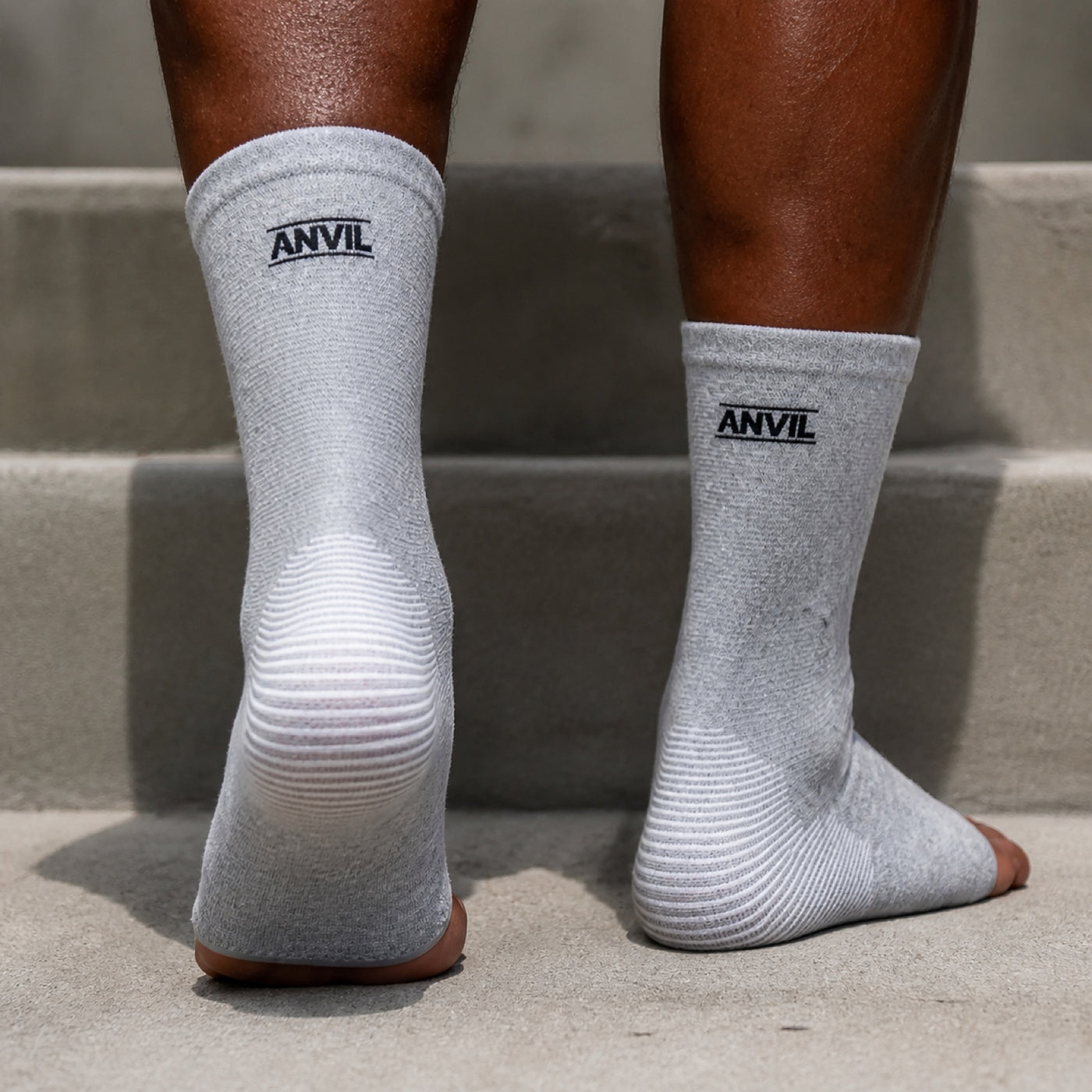 Close rear view of both heels in gray ANVIL foot sleeves on a concrete step, showing the ribbed heel panel.