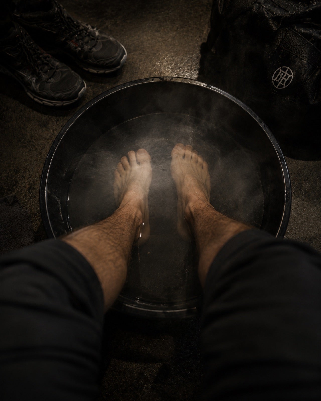 Bare feet in a steaming black basin, work boots and an ANVIL gym bag on the floor