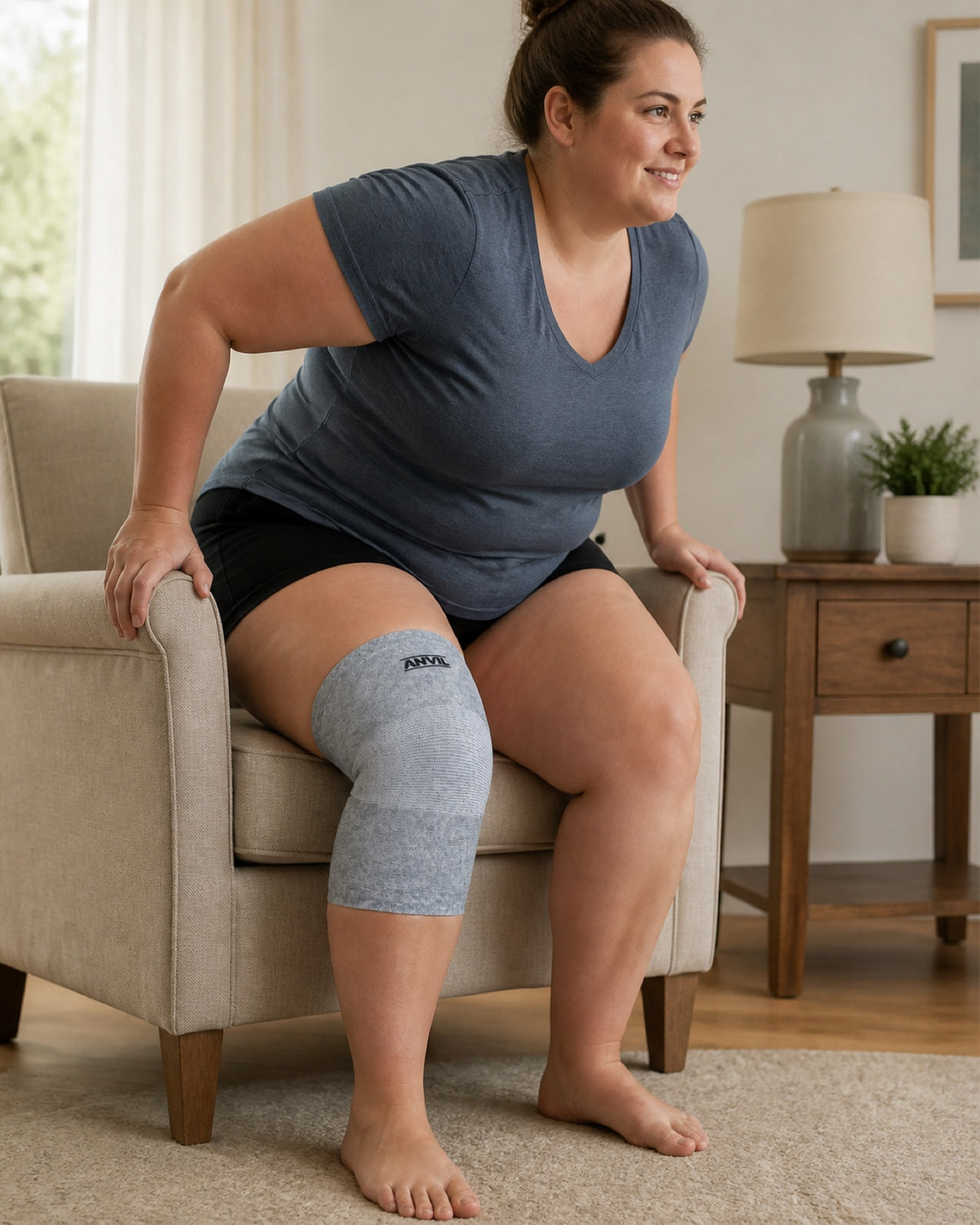 Woman rising from an armchair in a living room, with a gray ANVIL knee sleeve on her knee.