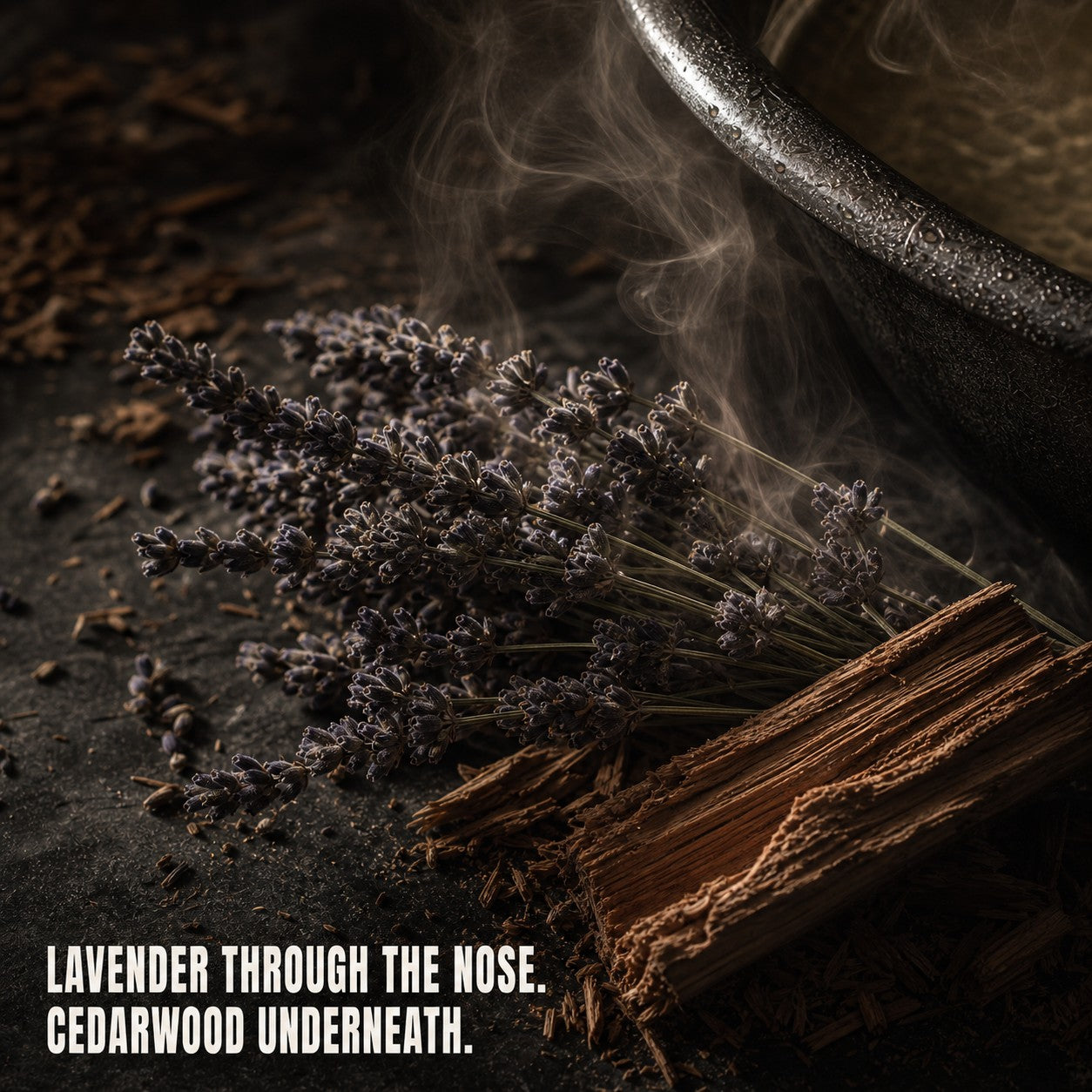 Dried lavender across split cedarwood beside a steaming gunmetal basin