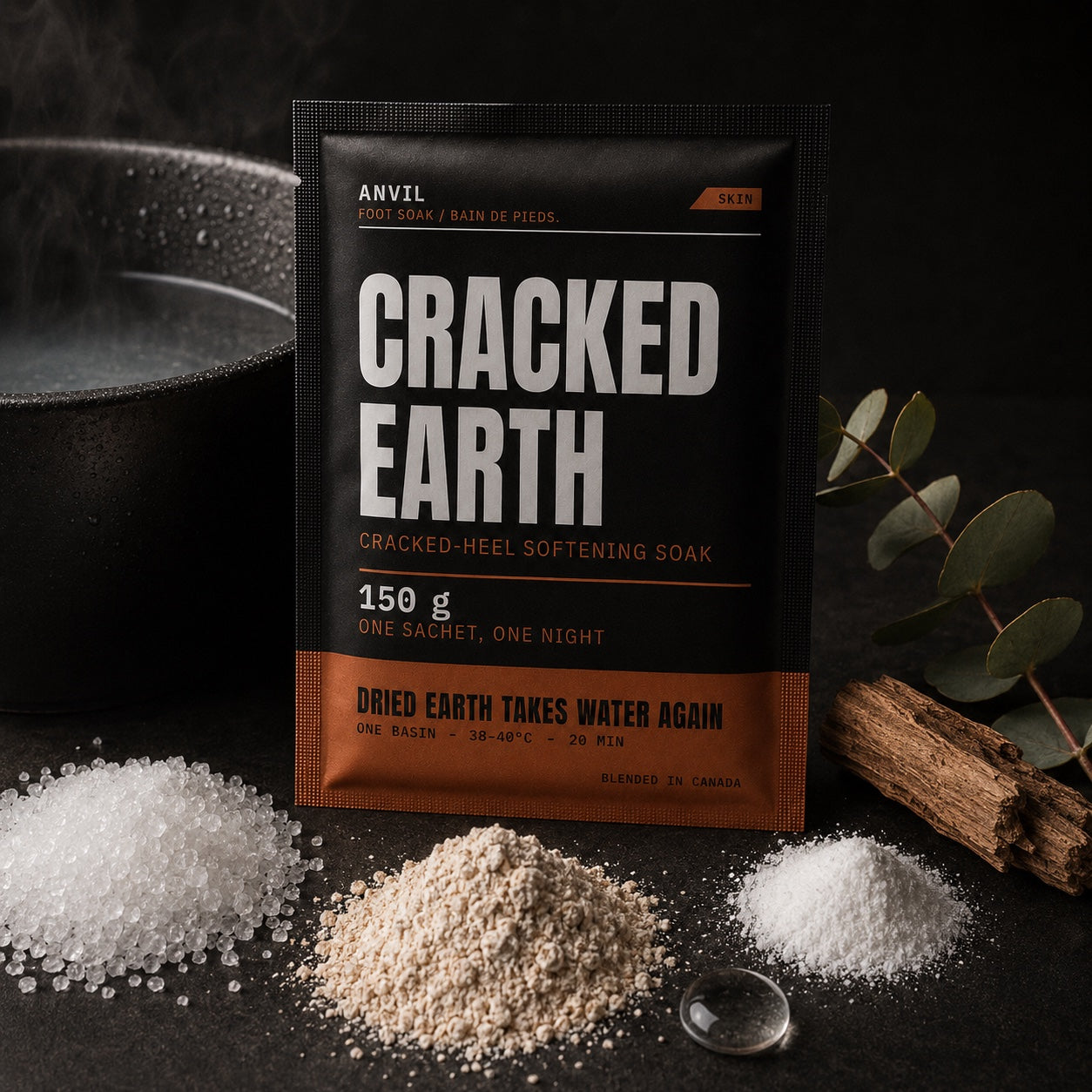CRACKED EARTH sachet with its raw ingredients &mdash; Epsom salt, colloidal oat, baking soda, glycerin, eucalyptus and cedar &mdash; beside a steaming gunmetal basin